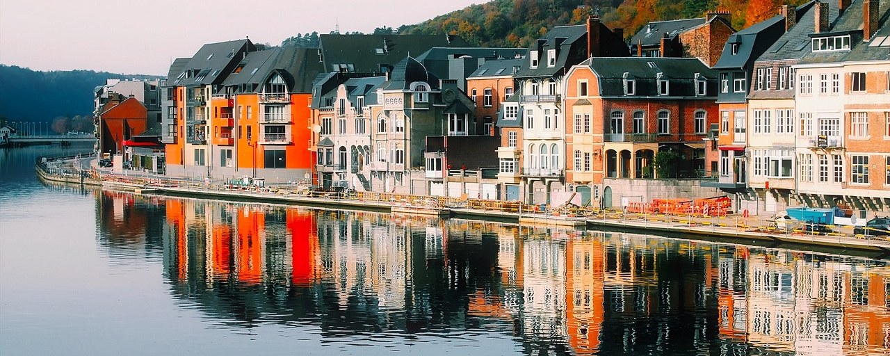 Colorful waterfront houses reflected in the Meuse River in Dinant, Belgium.