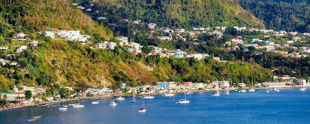 Coastal village and sailboats beneath forested hills on Dominica’s Caribbean coast