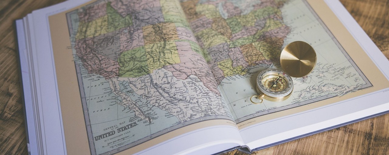 An open atlas with a brass compass resting on the page