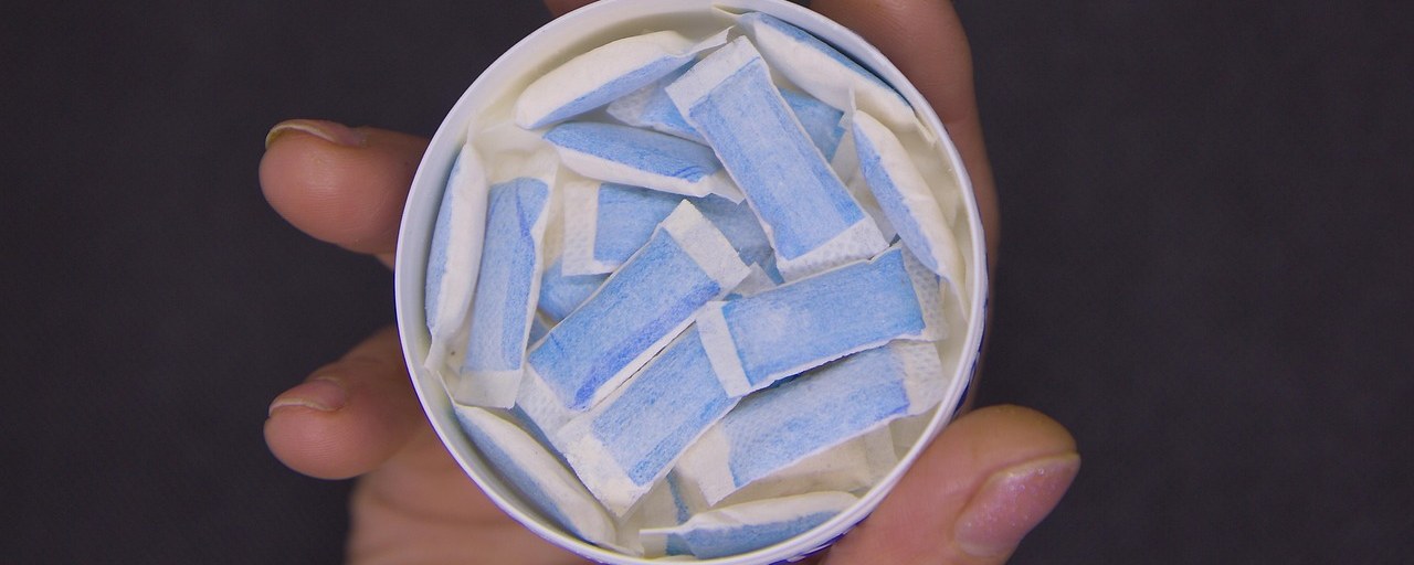 An open can of white nicotine pouches held in a hand