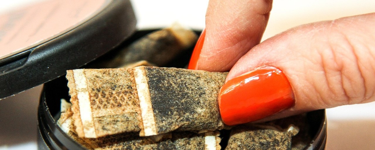 A hand lifting a portion of tobacco snus from an open can