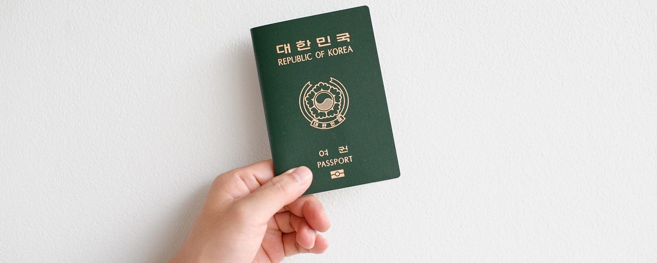 Hand holding a closed Korean passport against a plain wall