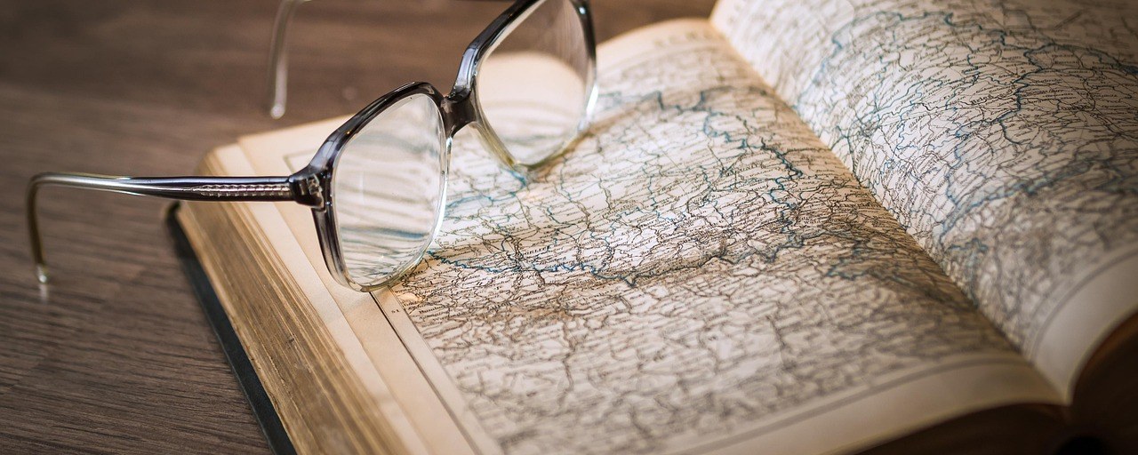 Reading glasses resting on an open atlas on a wooden desk